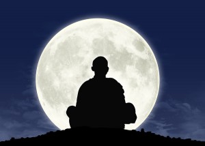 Silhouette of person meditating in front of a full moon